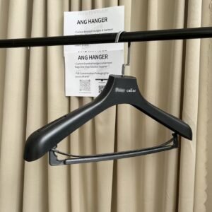 Black wood grain wholesale plastic clothes hanger with trouser bar and square metal hook, custom brand logo, hanging on clothing rack for apparel retail display