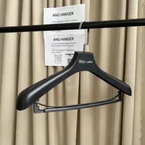 Black wood grain custom plastic hanger with non-slip shoulder ridges and trouser bar, engraved brand name, square chrome hook hanging on clothing rail for apparel retail