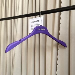 Purple non-slip plastic hanger for shirts and wedding dresses, textured shoulder grips with strap notches, chrome swivel hook with custom brand logo, hanging on clothing rod for apparel retail wholesale