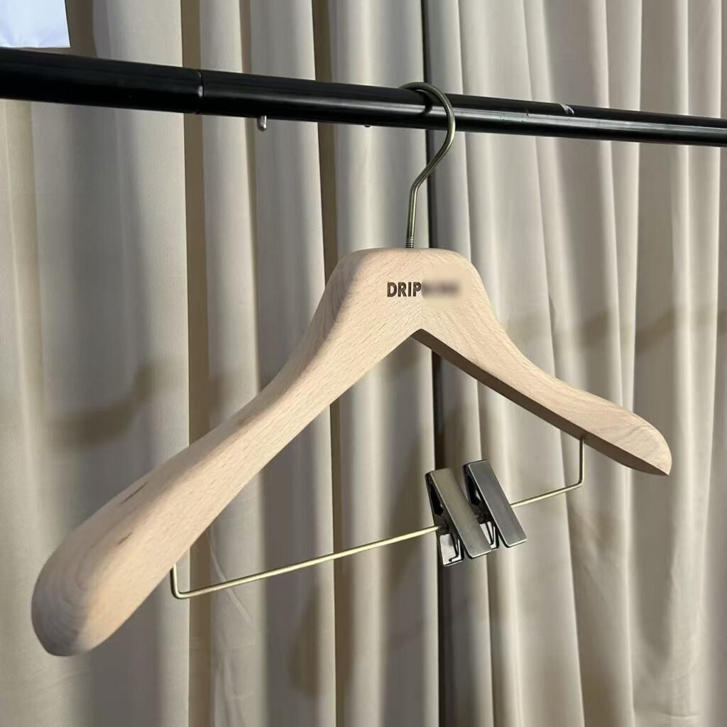 Natural beech wholesale wooden hangers with wide shoulder design, brass metal trouser bar with adjustable clips and custom engraved brand logo, premium suit and pant combo hanger for apparel boutique and retail display