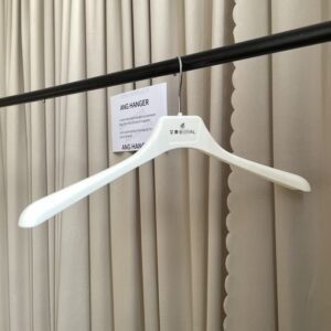 White smooth contoured hangers for shirts with chrome swivel hook and custom printed brand name, hanging on black clothing rail with supplier card against beige pleated curtain for wholesale apparel display