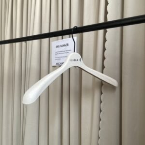Angled front view of multi shirt hangers with textured surface and black swivel hook, custom brand marking on the neck, hanging on black clothing rail with supplier info card against pleated curtain for apparel wholesale