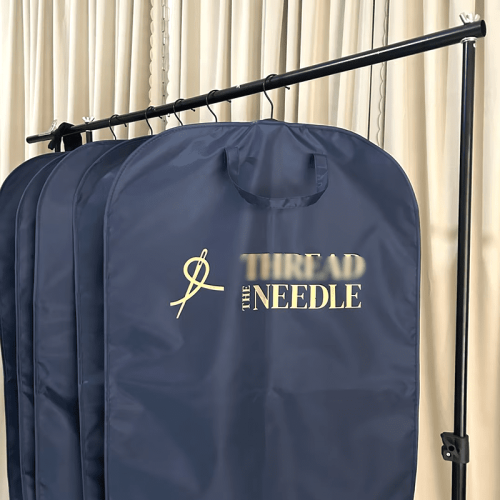 Navy clothing garment bags wholesale with custom printed gold brand logo, hanging in bulk on rack for boutique retail stock and suit garment storage